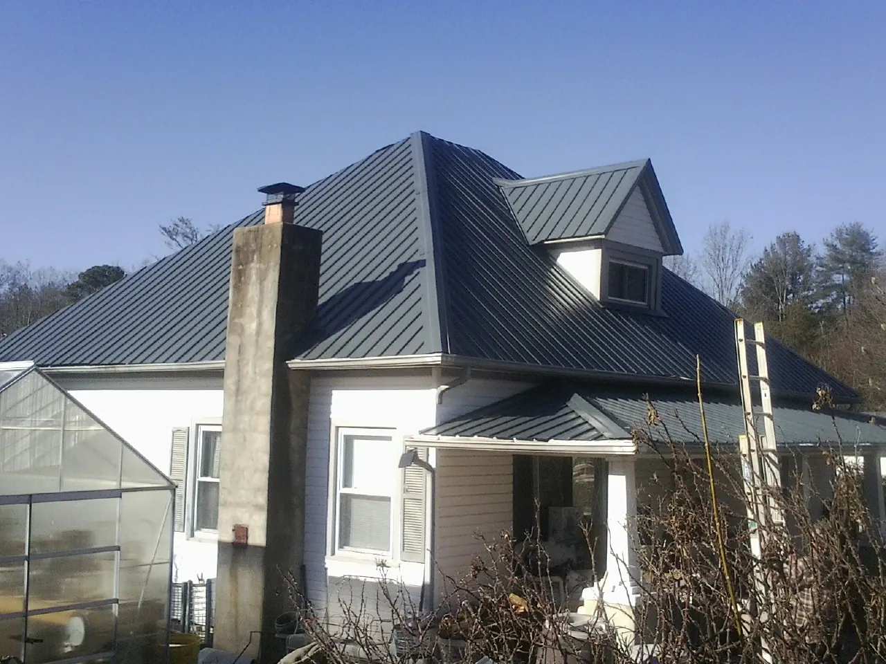Dark blue standing seam metal roof on a white farmhouse with dormer — Slate & Tile Roof Repair by Roofing Brothers in Townville
