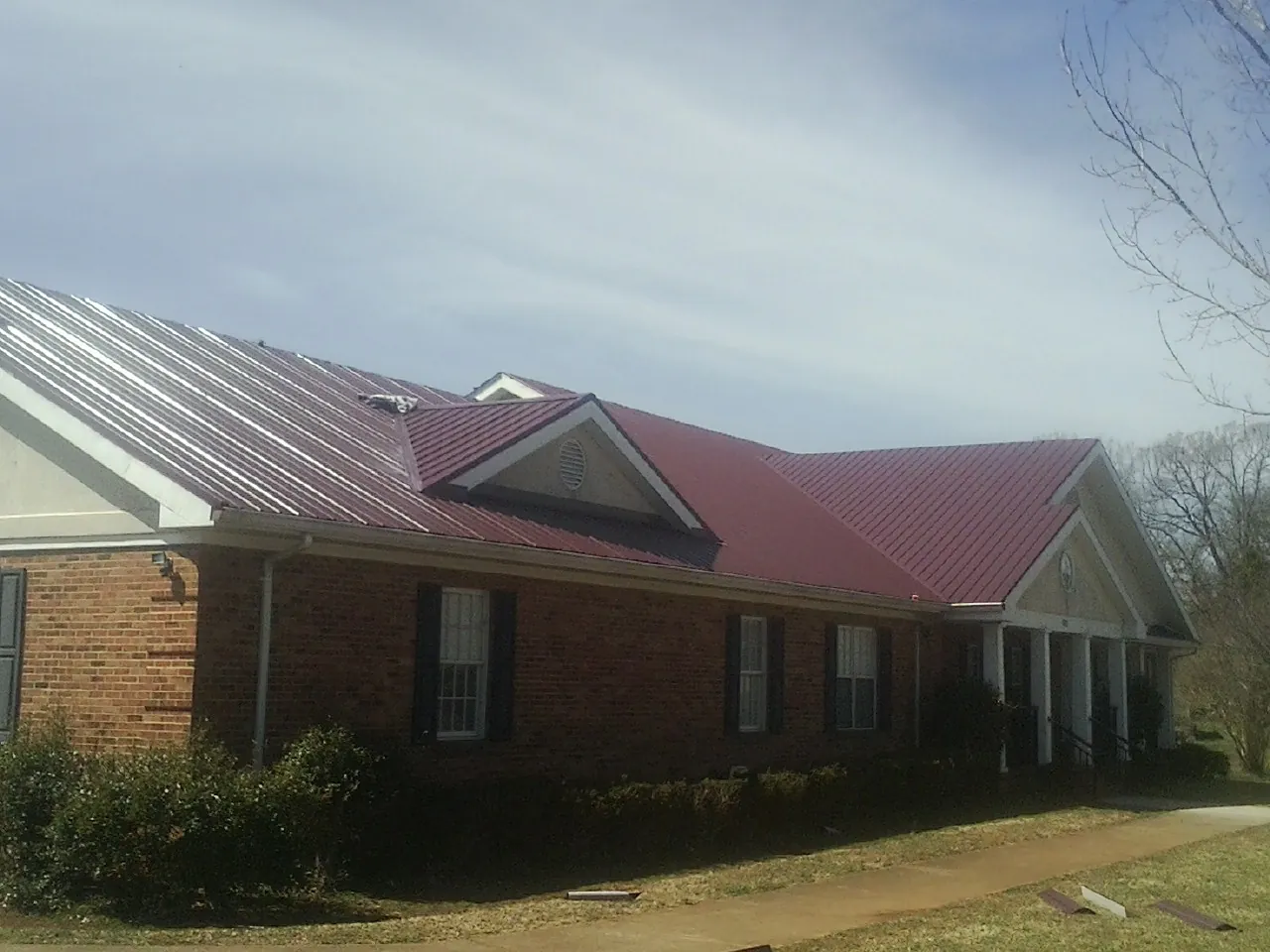 Red metal roof with gabled entries on a long brick building, from a Hail Damage Roof Repair job in Townville