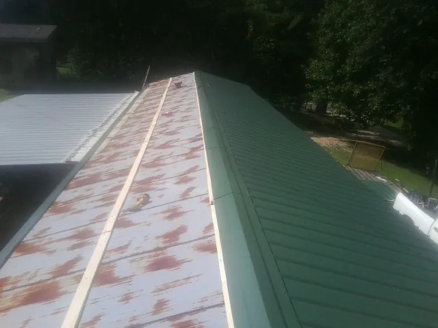 Old rusted panels beside newly installed green metal roofing — Wind Damage Roof Repair by Roofing Brothers in Townville