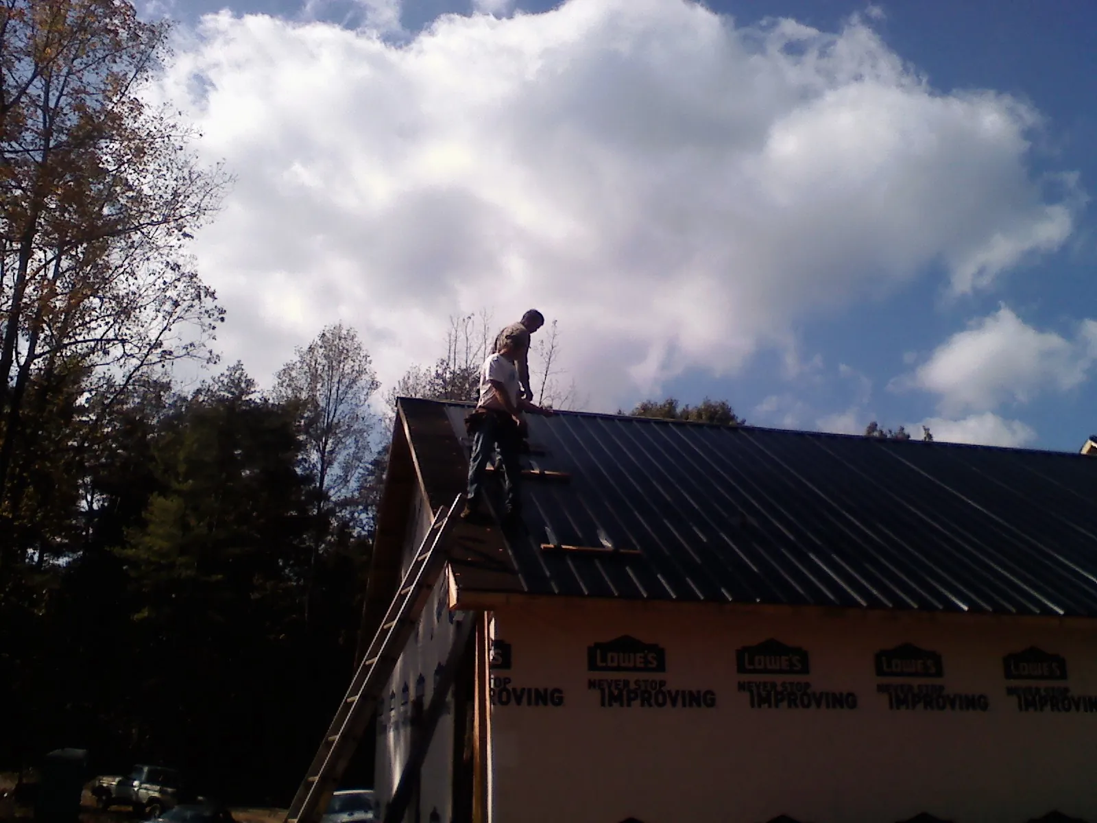 Roofer fastening dark metal panels high against a cloudy sky, from a Roof Inspection job in Townville