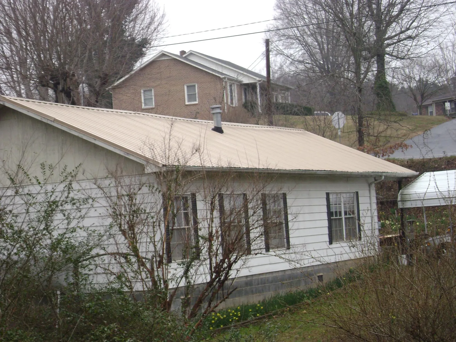 Tan metal roof on a white sided house set into a hillside — Commercial Roofing by Roofing Brothers in Townville